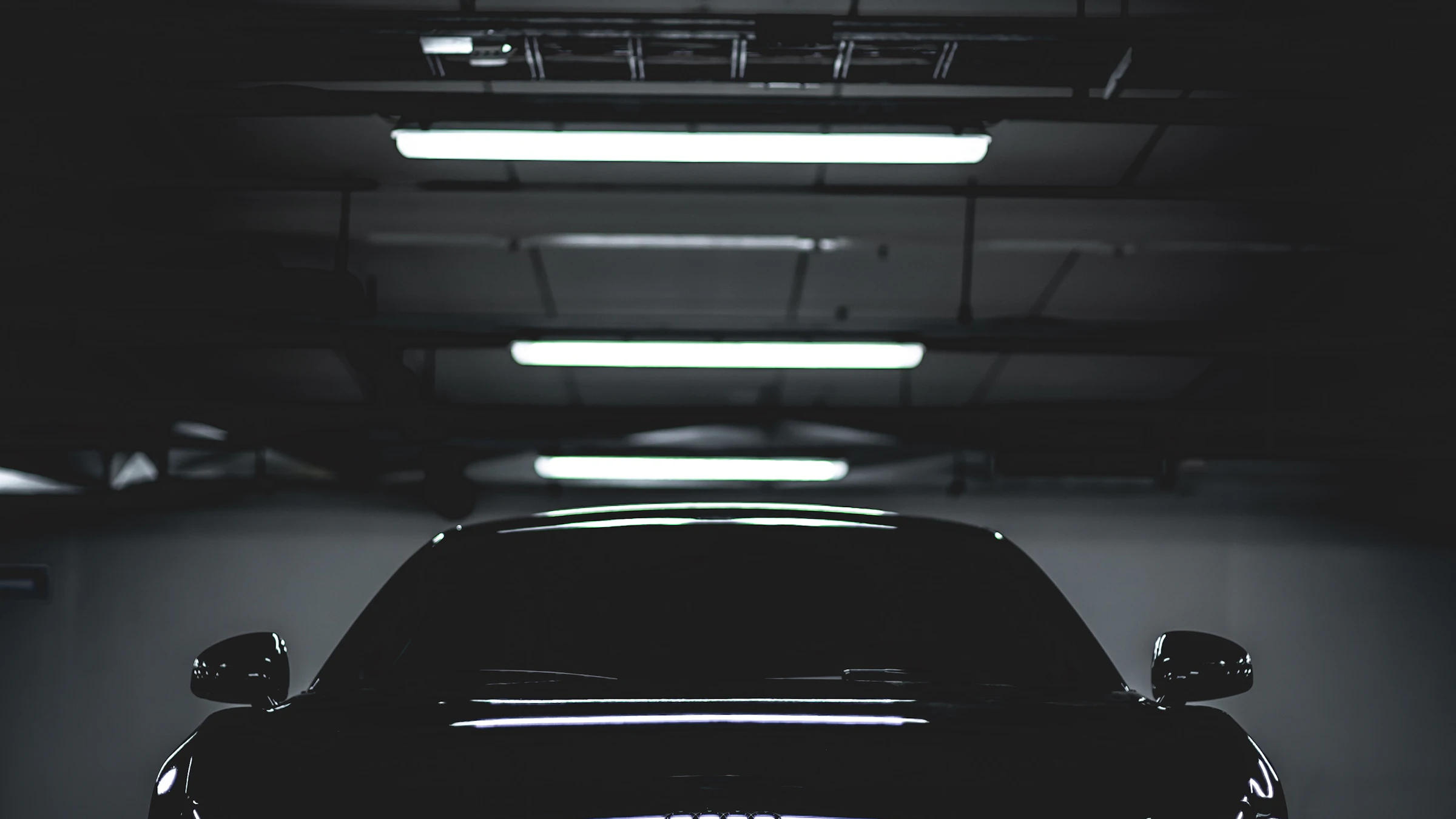 A car parked under work lights inside a dark garage bay